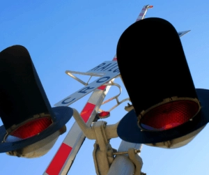 Railway level crossing warning lights and signal post viewed from below against a blue sky