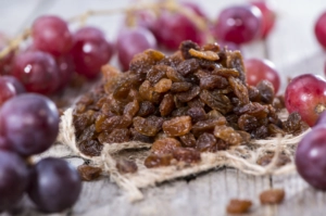 Close-up of a small pile of raisins on a piece of burlap fabric with fresh red and purple grapes scattered nearby
