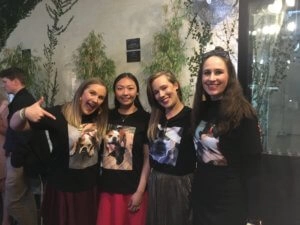 Xmas party group photo of four women wearing matching printed shirts standing together and smiling indoors